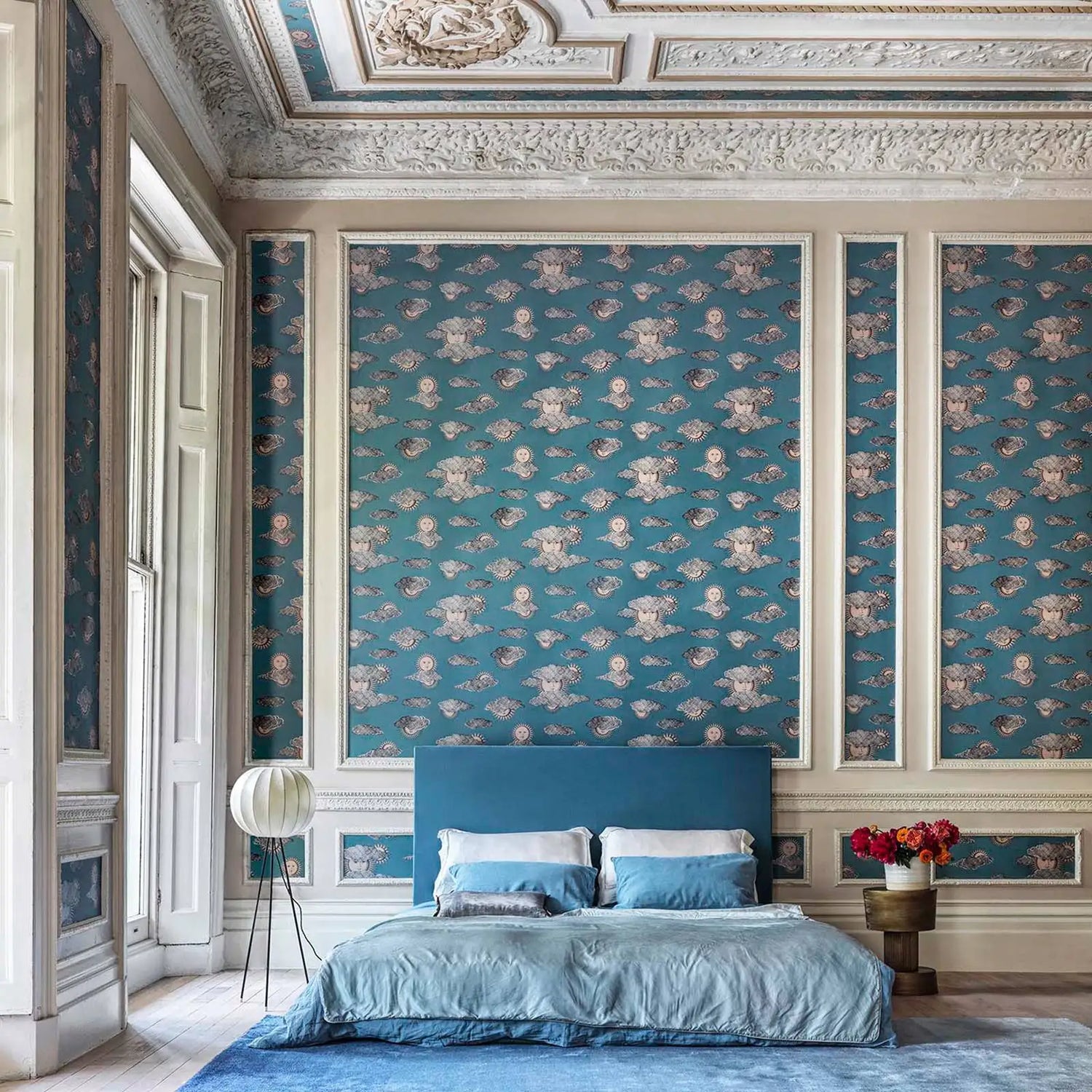 Luxurious bedroom with blue bedding and wallpaper, featuring intricate ceiling details.