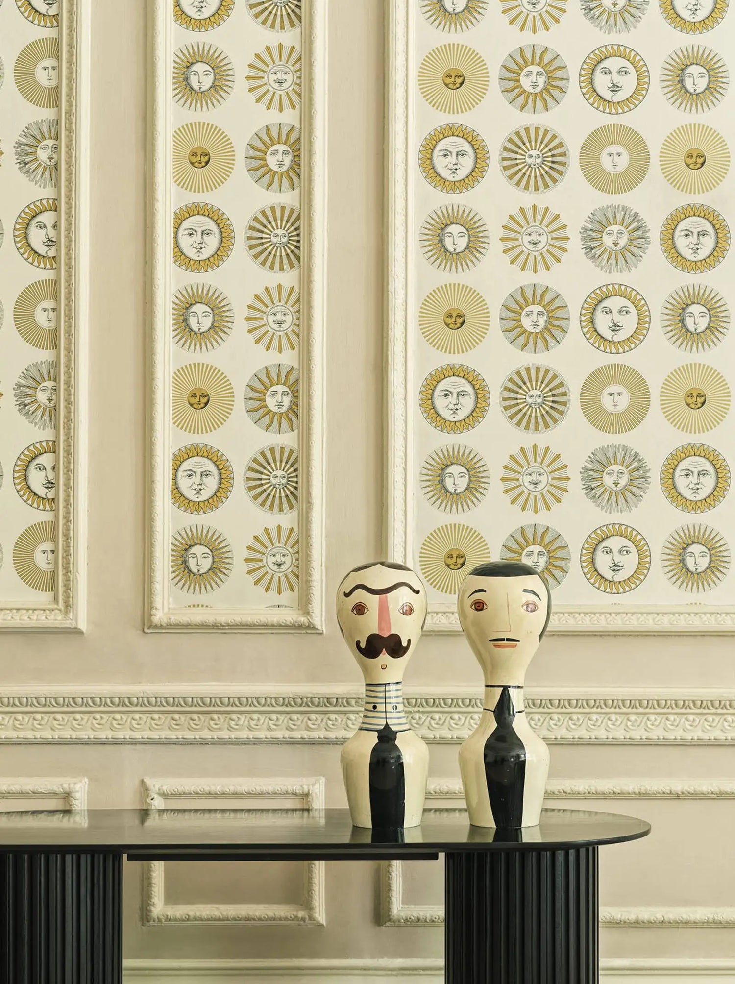 Decorative wall with sunburst pattern and two wooden figures on a table.