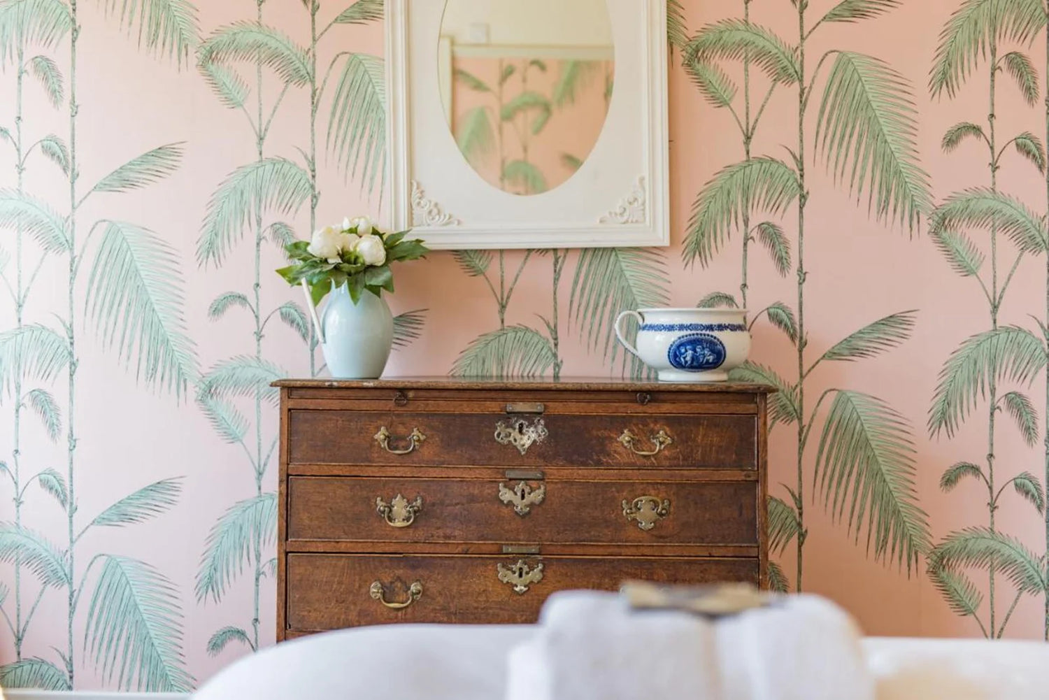 Wooden dresser with decorative items against a wall with palm leaf pattern