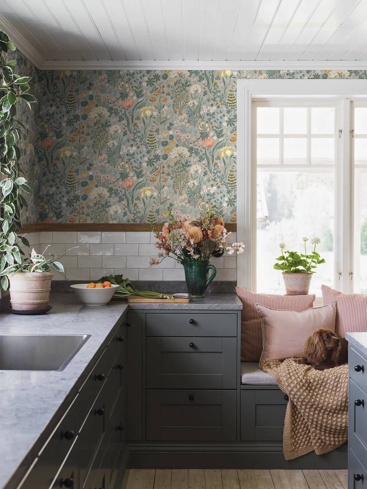 Kitchen with floral wallpaper, gray cabinets, and a window seat with pillows.