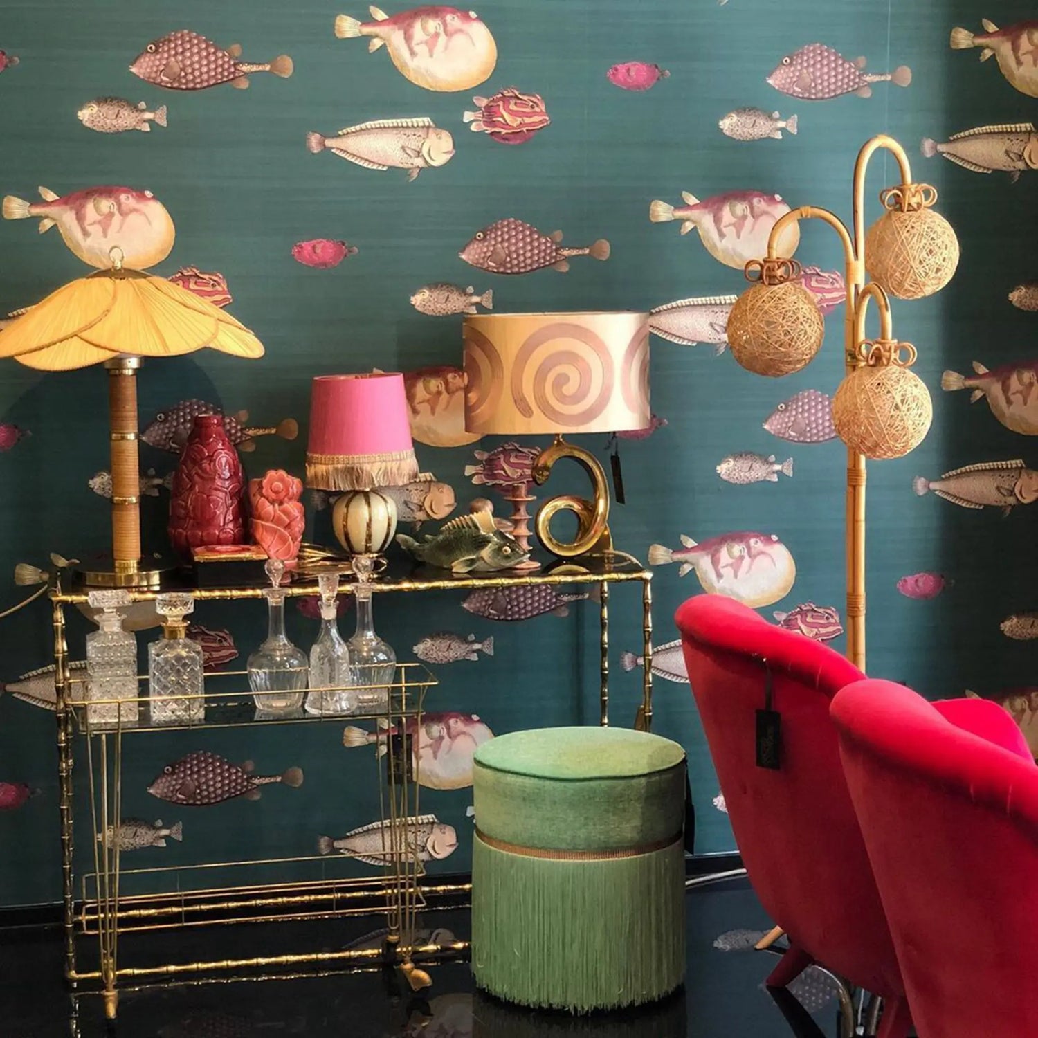 Decorative room interior with a gold bar cart, colorful lamps, and a red chair against a fish-patterned wall.