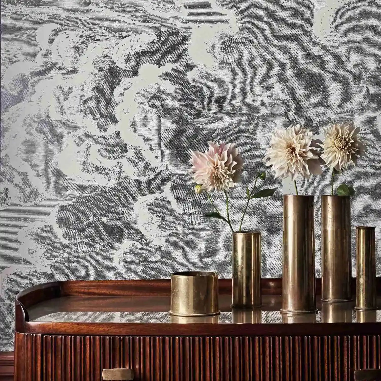 Decorative wall with cloud pattern, wooden console table with brass vases and flowers.