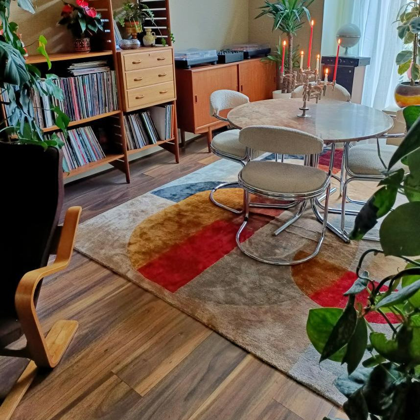 Dining area with a round table and chairs on a patterned rug, surrounded by books and plants.