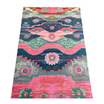 Colorful hand-tufted rug featuring Aztec geometric designs and floral medallions in shades of pink, teal, green, and dark blue.