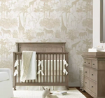 A styled nursery interior featuring a wooden crib with white bedding and tassels, a matching wooden dresser, and a wall covered in safari-themed wallpaper with giraffes, zebras, and palm trees.