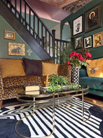 Living room with colorful decor, including a staircase, framed pictures, art deco black and white rug, and a coffee table.