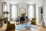 Living room with a piano, green chairs, and decorative blue rug.