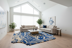 Modern living room with gray sofas, a blue and white patterned rug, and large windows.