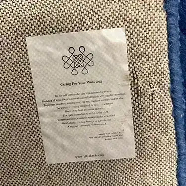Close-up view of the back of the Blue Arctic Geo Modern Hand Tufted Wool Rug, highlighting the detailed weave and care instructions. Perfect choice for rugs for living room or dining room, this wool rug combines style and durability.