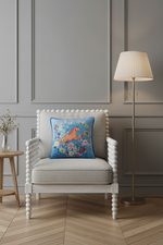 A decorative throw pillow with a colorful floral and horse design sits on a light gray upholstered armchair in a styled room with a floor lamp, wooden wall paneling, and a herringbone wood floor.