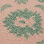 Close-up of a textured rug with a dusty pink background and a muted sage green geometric medallion pattern.