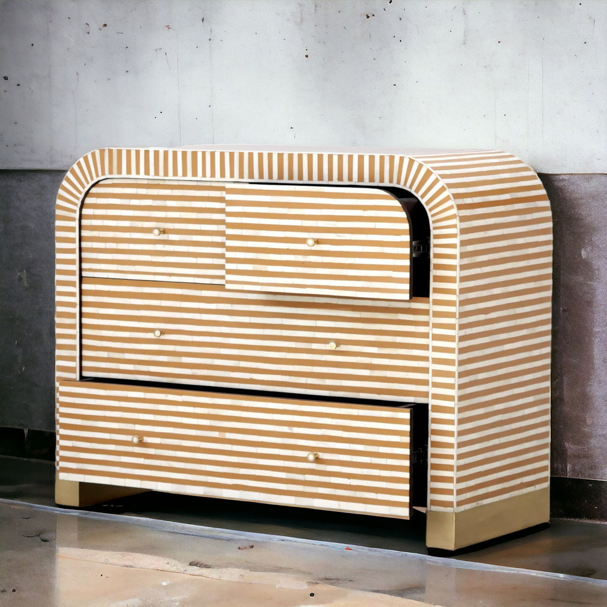 A modern three-drawer dresser with a curved top and bottom, covered in light natural wood and white horizontal stripes, set against a gray concrete wall.