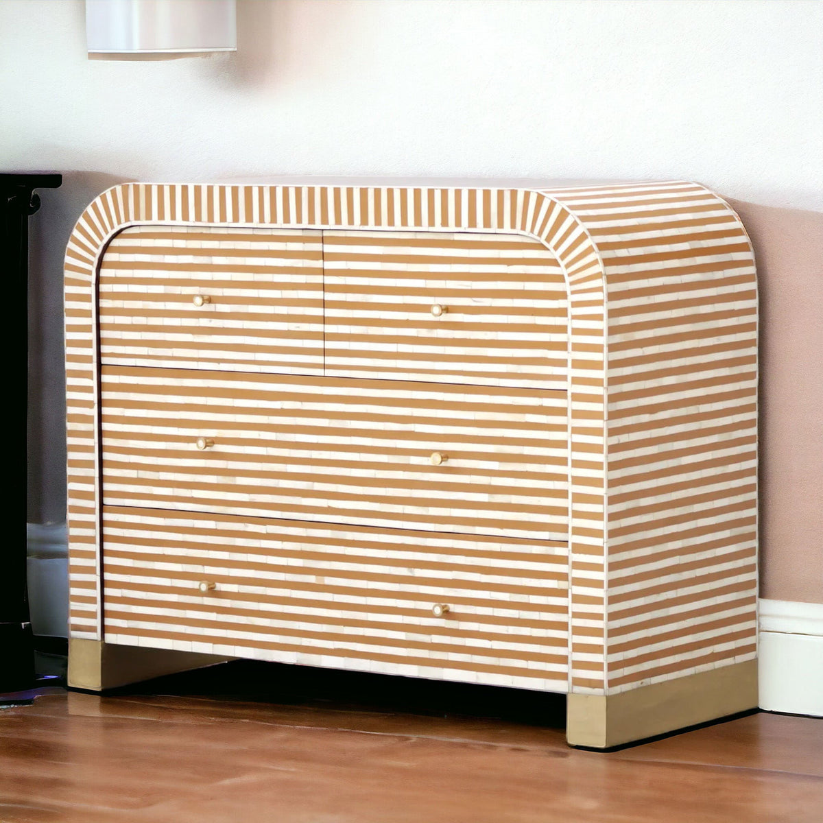 A modern chest of drawers with a curved top and front, covered in horizontal beige and white stripes, set against a neutral wall on a wooden floor.