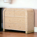 A modern chest of drawers with a curved top and front, covered in horizontal beige and white stripes, set against a neutral wall on a wooden floor.