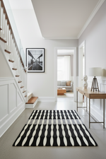Modern interior with a black and white striped rug, staircase, and living room.