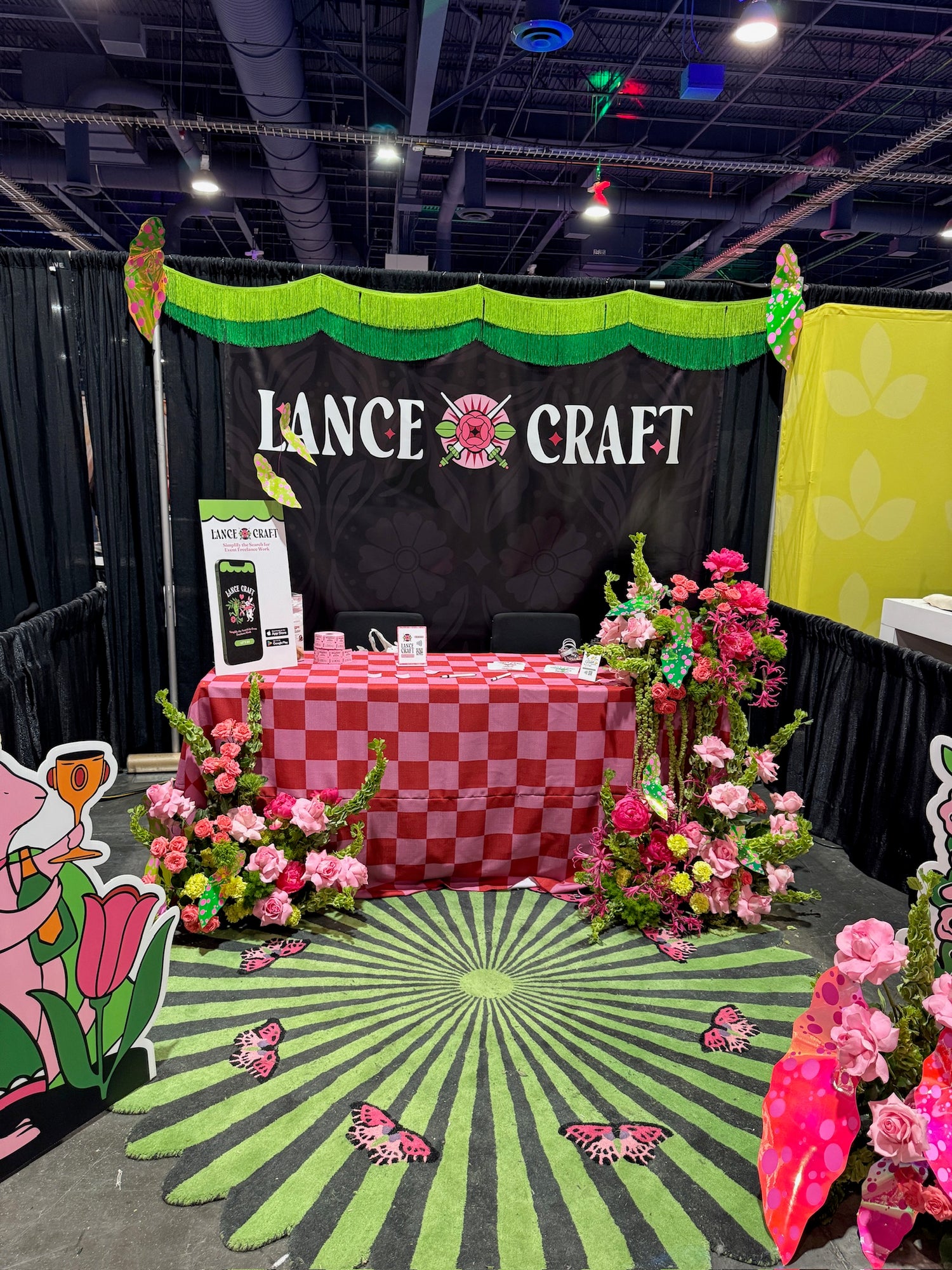 Decorative booth with 'Lance Craft' branding at a convention, featuring flowers and checkered tablecloth.