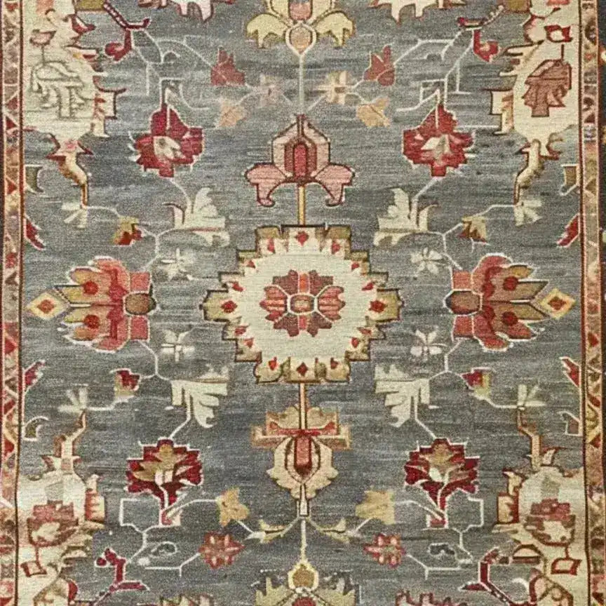 Elegant hand-knotted area rug featuring a charming floral cascade design. The intricate patterns in hues of red, pink, and cream stand out against a muted grey background, adding a touch of sophistication and warmth to any room.