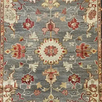 Elegant hand-knotted area rug featuring a charming floral cascade design. The intricate patterns in hues of red, pink, and cream stand out against a muted grey background, adding a touch of sophistication and warmth to any room.