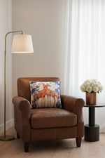 A square decorative throw pillow featuring an illustration of two giraffes, styled on an olive green velvet sofa in a modern living room setting.