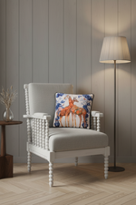 A square decorative throw pillow featuring an illustration of two giraffes, styled on an olive green velvet sofa in a modern living room setting.