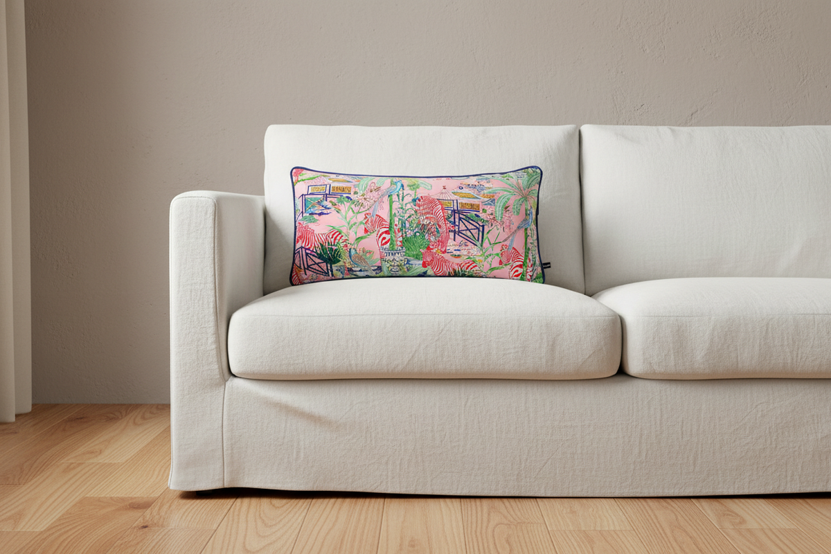 A square decorative throw pillow with a vibrant multicolor floral and botanical print, featuring a dark green border, styled on a white slipcovered sofa in a modern living room setting with light wood floors.