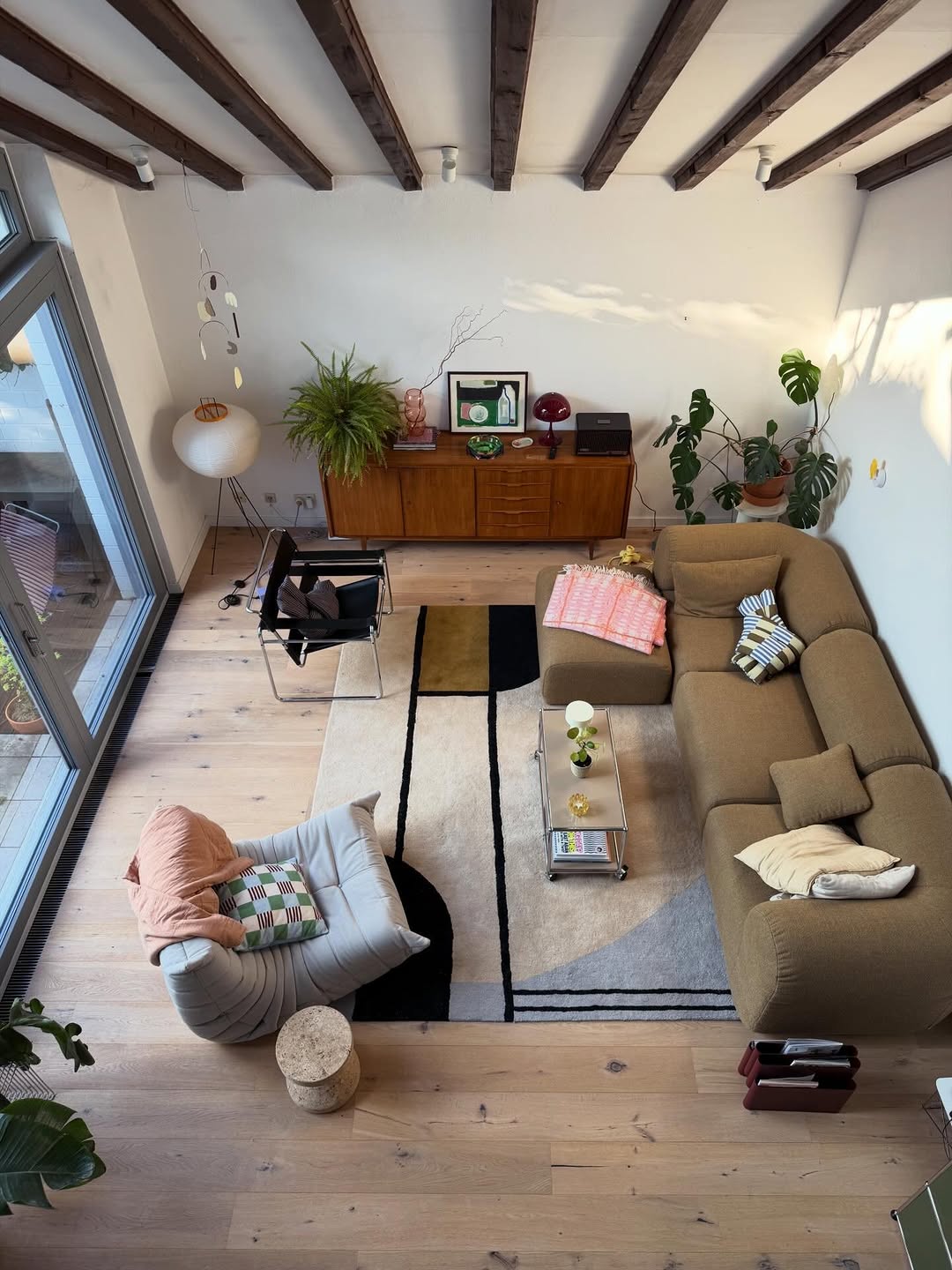 Modern living room with wooden floor, brown rug, sectional sofa, and decorative elements.