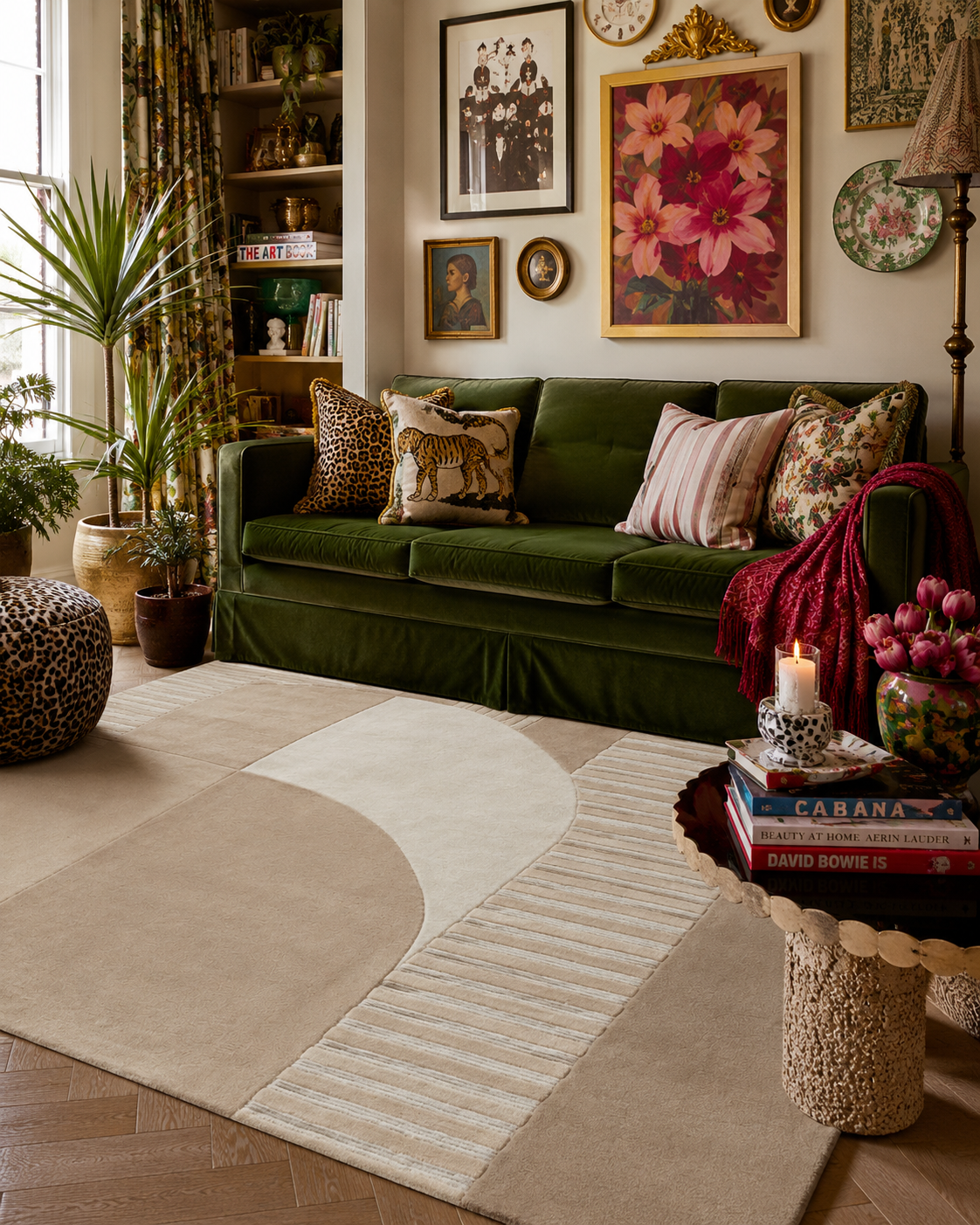 A styled living room featuring a large abstract area rug in beige and cream tones, a deep green velvet sofa with patterned pillows, and a decorative side table in the foreground.