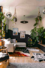 A stylish living room featuring a modern area rug with a bold, abstract design. This wool rug, perfect for any contemporary setting, is placed under a cozy sectional sofa. The space is accented with lush greenery and framed artwork, highlighting the area rugs for living room.