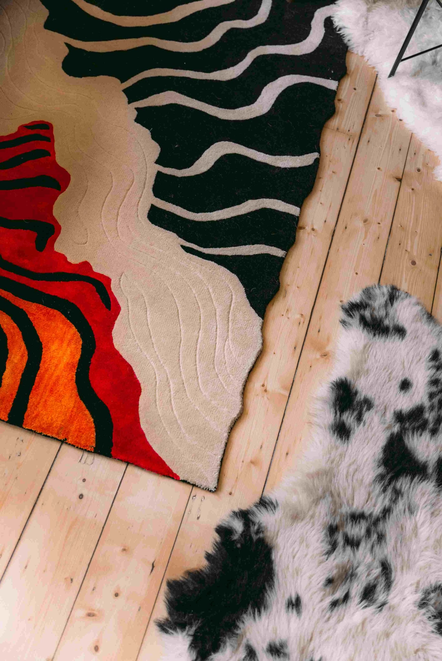 A stylish area rug with a striking abstract design in red, black, and beige hues, perfect for a contemporary living room. The hand-tufted wool rug adds a modern touch to the wooden floor, enhancing the look of this living space.