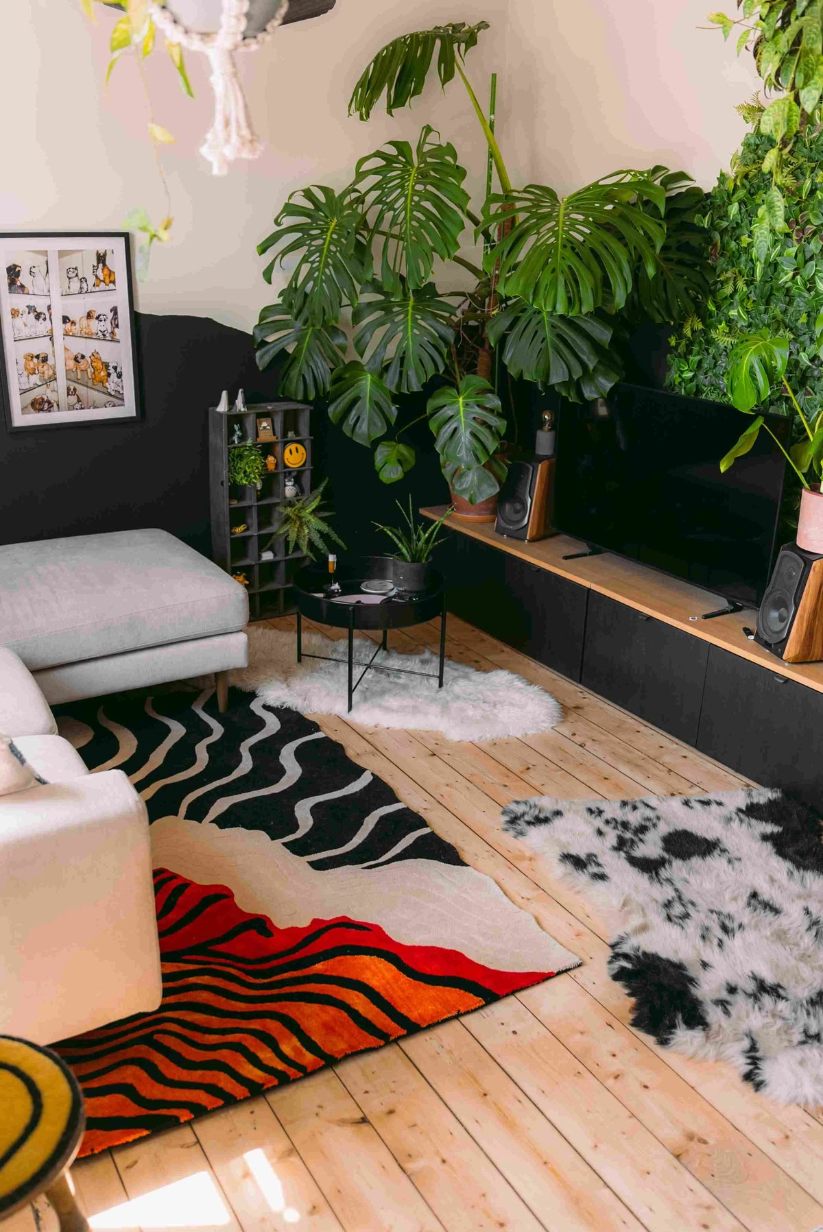 A contemporary area rug with bold, curved lines in shades of black, red, and orange, adding a vibrant touch to a cozy living room. The wool rug complements the natural wood flooring and lush green plants, creating a warm and inviting space. Ideal for those seeking stylish area rugs for living room decor.