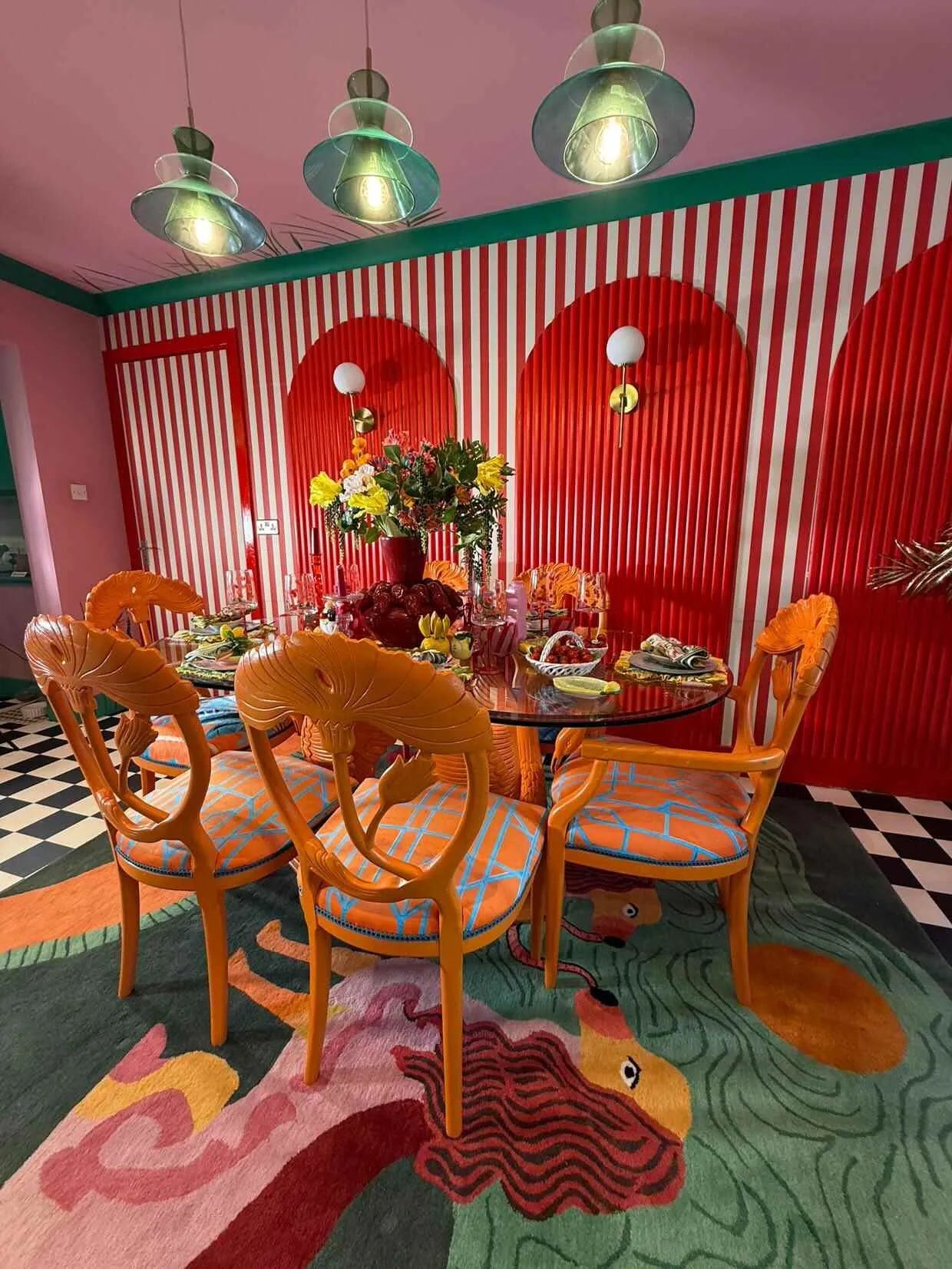 Vibrant dining room featuring a Duo Tails Hand Tufted Area Rug with abstract design under a glass table surrounded by orange chairs. Ideal for a contemporary touch in a bedroom or office, this wool rug adds a bold statement to any space.