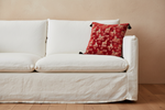 An olive green sofa in a modern living room setting, styled with a red patterned throw pillow and a black side table holding a black vase with dried branches.