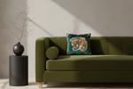 An olive green velvet sofa in a modern living room setting, styled with a round cylindrical bolster pillow and a square decorative throw pillow featuring a colorful tiger print. A black textured side table with a black vase and dried branches stands to the left against a textured beige wall with diagonal sunlight shadows.