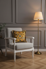An olive green fabric loveseat sofa in a styled living room setting, featuring a decorative yellow and blue patterned throw pillow, a textured gray wall with hexagonal wall art, and a floor lamp.