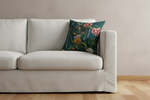 A white spindle-arm accent chair with a light beige upholstered seat and back, styled with a dark teal floral throw pillow. The chair is set in a bright, modern room with light wood herringbone flooring, a gray paneled wall, a floor lamp, and a small side table.