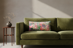 A brown leather wingback armchair with a matching ottoman in a warm, styled room. A colorful floral accent pillow rests on the chair, alongside a floor lamp and a side table with a vase of white flowers.