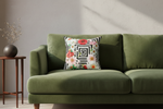 An olive green velvet sofa in a styled living room setting, featuring a square throw pillow with a black geometric maze pattern and a colorful floral border.
