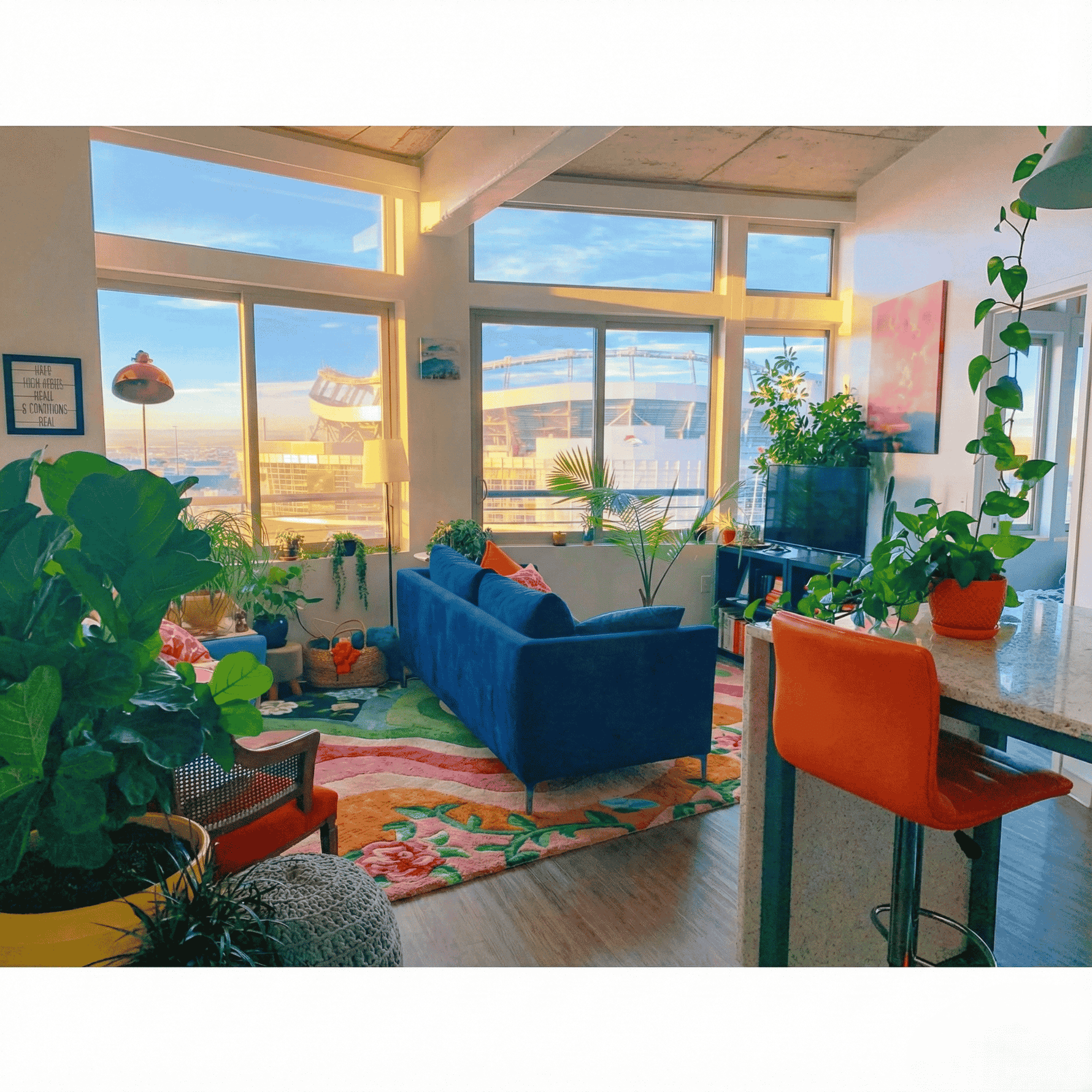 Modern living room with blue sofa, orange chair on a rug and large windows.