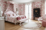 Pink and white bedroom with round floral rug, floral patterns on walls, bed, and curtains.