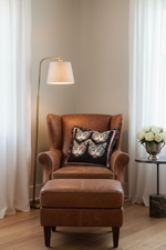 An olive green velvet sofa in a modern living room setting, styled with a square throw pillow featuring four illustrated cat faces on a black background with pink fringe.