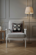 An olive green velvet sofa in a modern living room setting, styled with a square throw pillow featuring four illustrated cat faces on a black background with pink fringe.