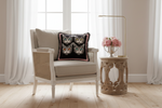 Four cats velvet throw pillow with fringe trim on a cream cane-back armchair beside a sunlit window.