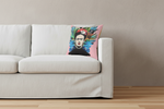 A square throw pillow featuring a colorful Frida Kahlo portrait print, styled on a light wood and cream armchair in a rustic room with a textured brown wall and wooden floor.