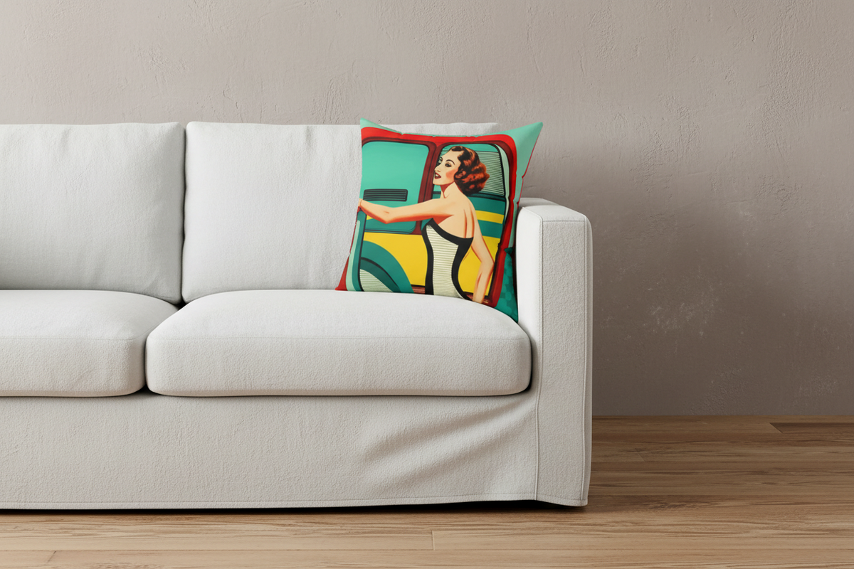 A square throw pillow featuring a retro-style illustration of a woman in a yellow dress leaning against a teal and red vehicle, styled on a white slipcovered sofa against a textured beige wall.