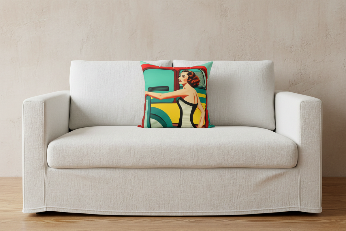 A square throw pillow featuring a retro-style illustration of a woman in a yellow dress leaning against a teal and red vehicle, styled on a white slipcovered sofa against a textured beige wall.