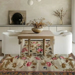 Elegant square hand-tufted wool rug with a floral design, perfect for a bedroom or large living room setting. This area rug features a beautiful blend of pink and brown flowers against a neutral background, enhancing the cozy ambiance of the space. The rug is paired with a wooden table and white chairs, showcasing its versatility and charm as a centerpiece in any living room.