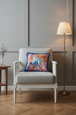 A light gray upholstered armchair with a colorful abstract horse-print throw pillow, set in a modern room with a wooden floor, a side table, and a floor lamp.