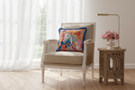 A beige upholstered armchair with woven cane sides sits in a bright room beside a carved wooden side table holding pink roses and a brass lamp. A colorful throw pillow with a blue border and horse-and-floral print rests on the chair.