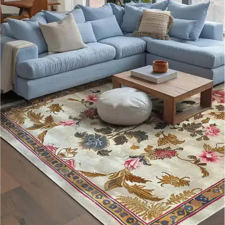 A beautifully designed Golden Glory Square Hand Tufted Wool Rug graces the floor of a cozy living room. The square area rug features an elegant floral pattern with vibrant colors, making it a perfect choice for bedrooms or large living rooms. The wool rug complements the light blue sectional sofa, creating a warm and inviting atmosphere, ideal for area rugs in living rooms.