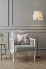 A light beige fabric slipcovered sofa with a decorative throw pillow featuring a leopard print, set against a textured beige wall and light wood flooring.